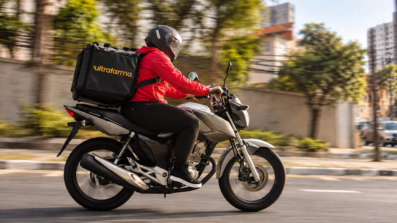 Entregador da Ultrafarma de moto, com bolsa térmica preta com a marca da farmácia